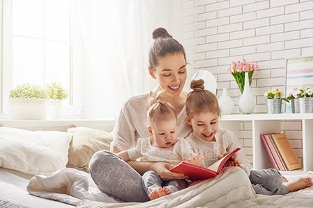 woman with children sitting on a bed reading a book